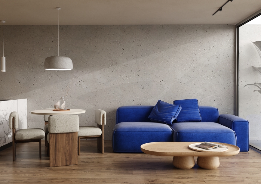 Sala do T2, com sofá azul, mesa redonda e parede em betão à vista